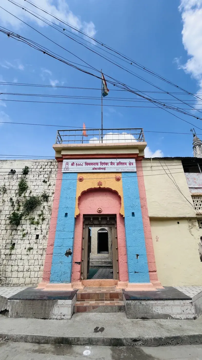 A wider view of the kshetra's entrance gate from the street, an orange flag flying from the rooftop railing above, overcast sky.