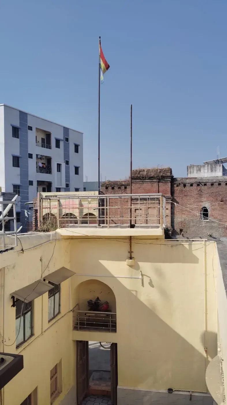 The entrance gate at street level, a motorbike parked beside it and the tip of the temple's white shikhar showing above the boundary wall.