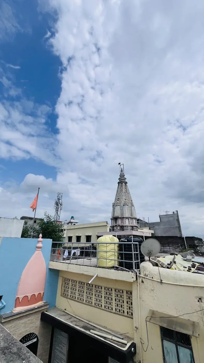 A rooftop view from the kshetra, flagpoles in the foreground and an old brick boundary wall stretching toward the neighbouring buildings.