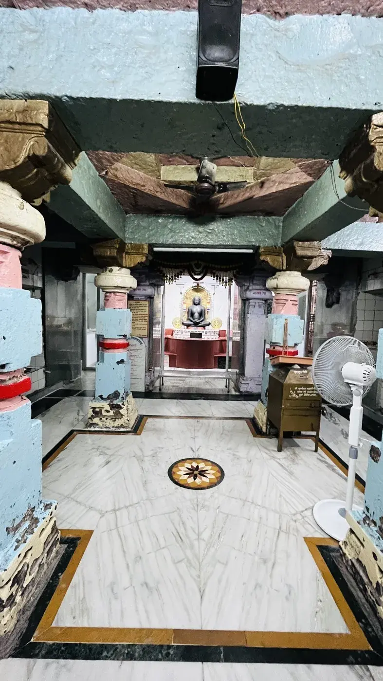 The garbhagriha seen from the mandap, pillars framing the red-toned vedi where the black stone Moolnayak murti sits enshrined.