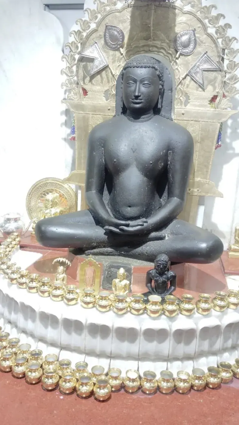 The Moolnayak murti during a ceremony, rows of small brass kalash set around its base and silver flags rising on either side.
