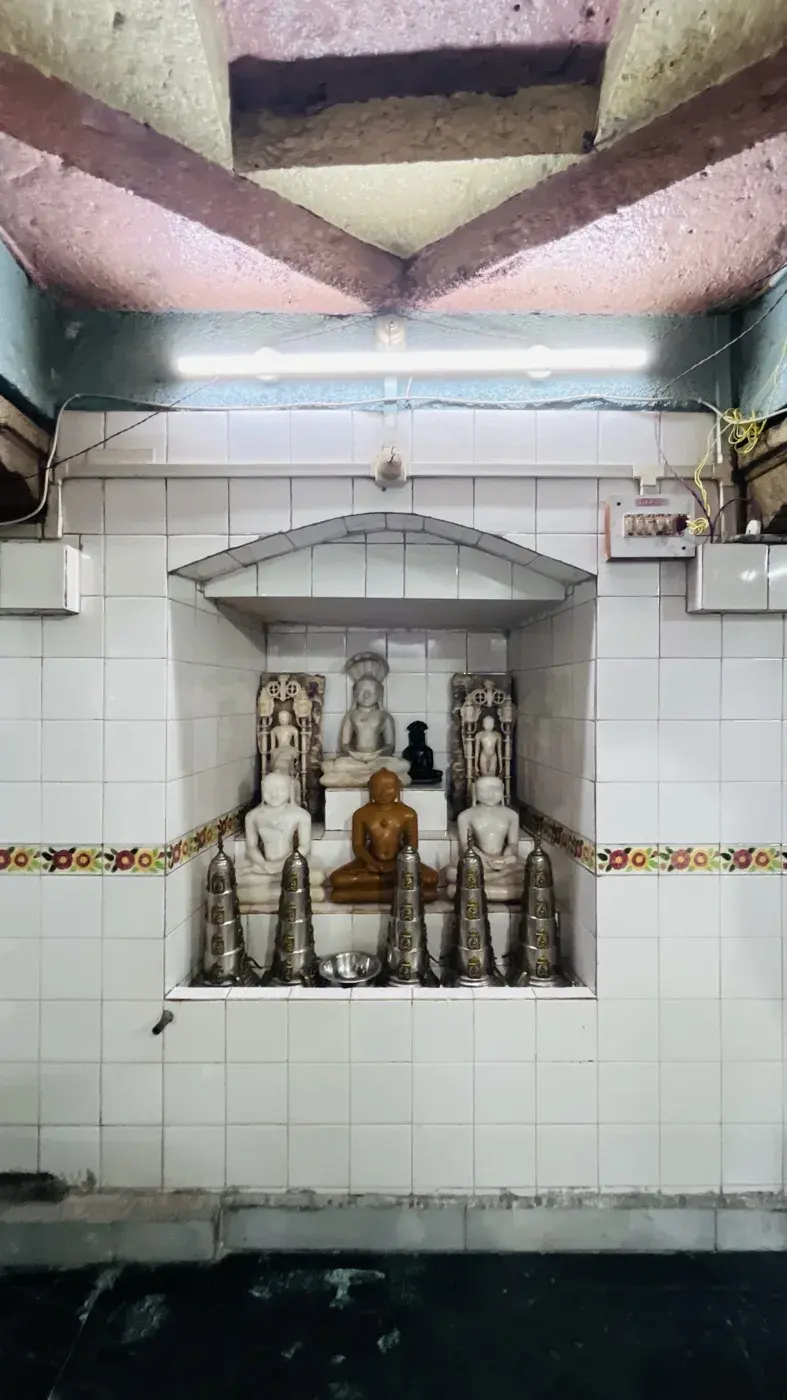 A tiled shrine niche with a group of Tirthankara murtis in white marble and polished wood, a row of silver bell-shaped covers set before them.