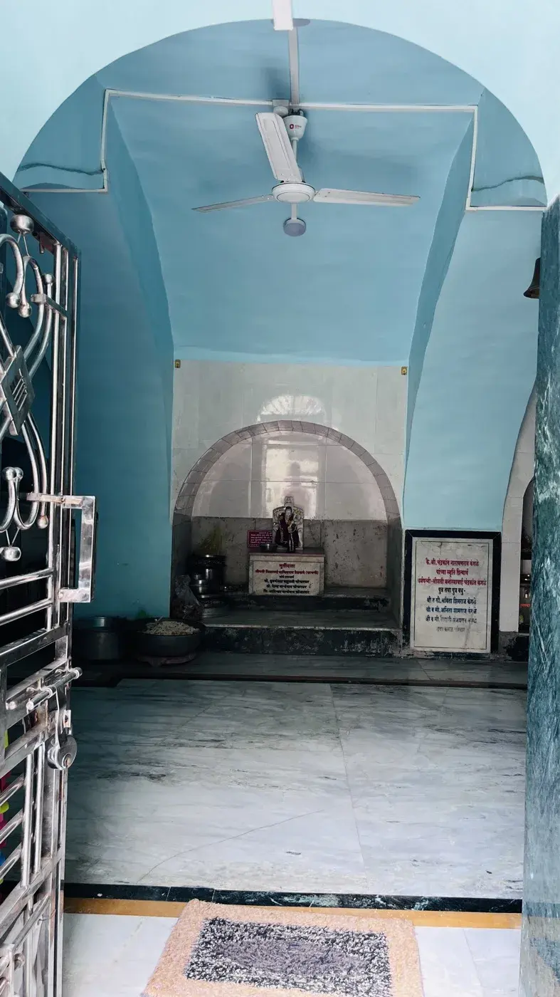 A small shrine niche beneath a blue arch, its murti draped in saffron cloth for worship.
