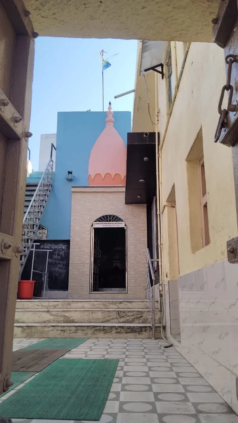 Looking out from the kshetra's inner doorway into a small courtyard, a metal staircase and a pink-domed subsidiary shrine against a painted blue wall.