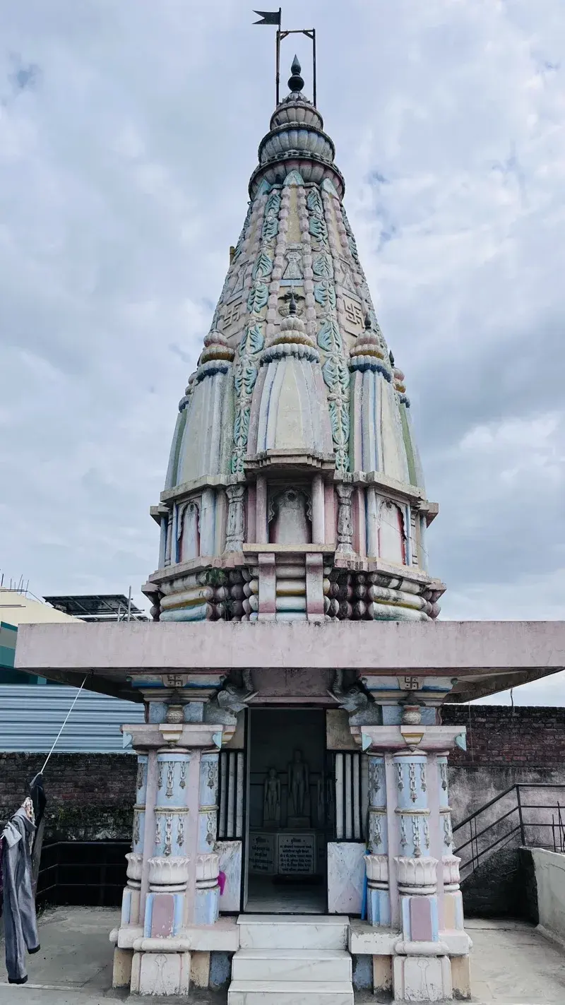 Through an elephant-carved doorway, a small marble shrine of three standing Tirthankara murtis on a pedestal inscribed with donor names.