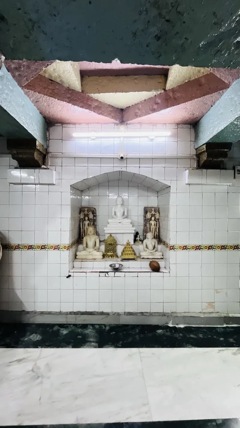 A tiled shrine niche holding a small group of Tirthankara murtis, a larger seated figure at the centre flanked by smaller images, with an offering bowl before them.
